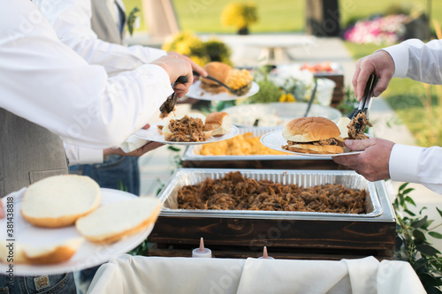 Close up of bridal party dishing up catered buffet food at casual outdoor wedding