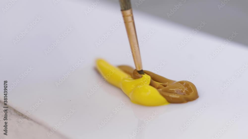 Close-up of artist using a brush to mix paint colors brown and yellow Close-up of artist using a brush to mix paint colors brown and yellow
