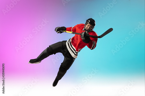 In flight. Male hockey player with the stick on ice court and neon gradient background. Sportsman wearing equipment, helmet practicing. Concept of sport, healthy lifestyle, motion, wellness, action.