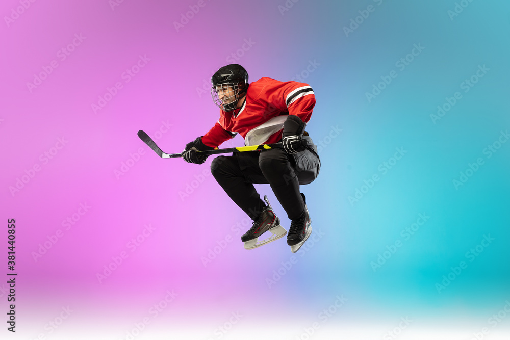 In jump. Male hockey player with the stick on ice court and neon gradient background. Sportsman wearing equipment, helmet practicing. Concept of sport, healthy lifestyle, motion, wellness, action.