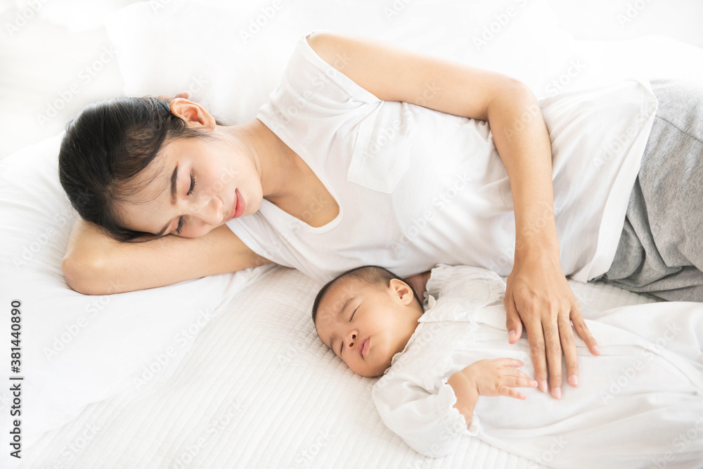 Beautiful asian women mother with long black hair in the white pajamas. Asia mom and newborn infant with love, while a baby sleeping in her arm with warm, safe, comforted resting on the clean bed. Beautiful asian women mother with long black hair in the white pajamas. Asia mom and newborn infant with love, while a baby sleeping in her arm with warm, safe, comforted resting on the clean bed.