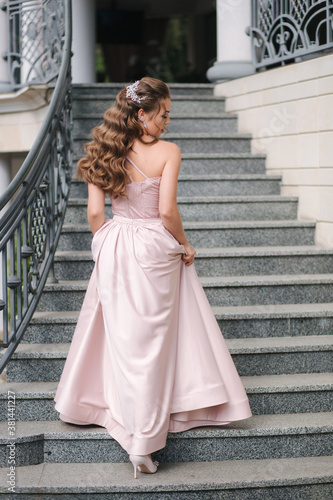 Beautiful girl with curly hair in evening dress stand on the stairs