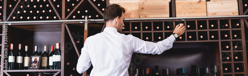 Panoramic shot of sommelier taking wine bottle from rack in restaurant