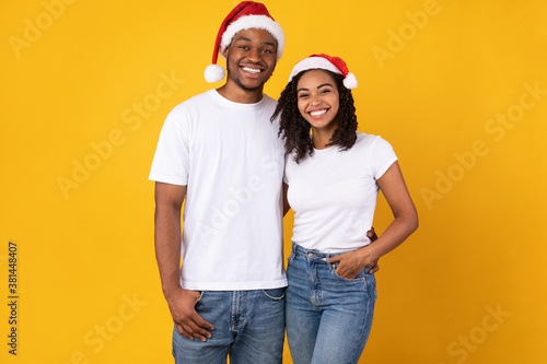 Joyful African Couple In Santa Christmas Hats Posing, Yellow Background © Prostock-studio