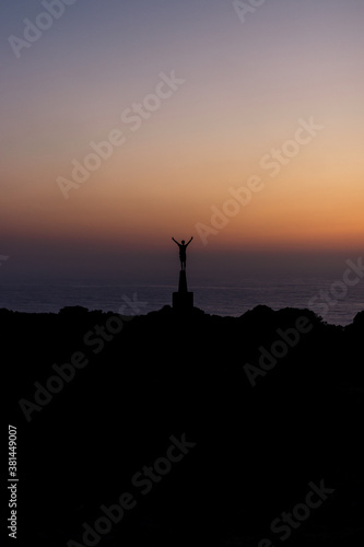 Silhouette of a young man with raised arms enjoying the freedom at the sunset with the sea in the background.