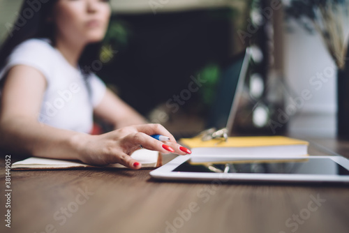 Crop female freelancer using tablet and taking notes at home