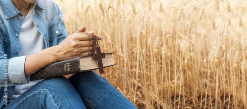 Foto Christian woman praying on holy bible and wooden cross in barley field on summer