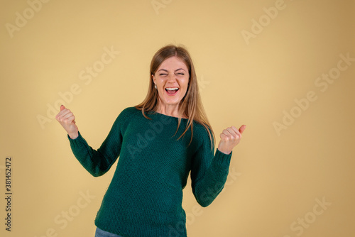 Lucky pretty young woman saying yes, everything worked out concept, isolated on yellow background