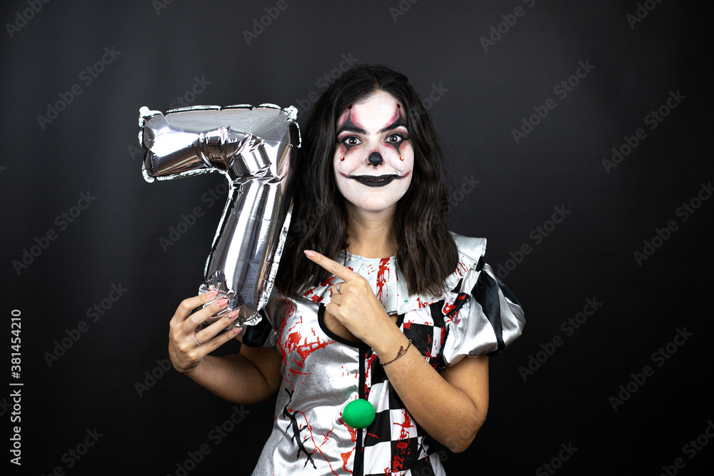 woman in a halloween clown costume over isolated black background holding a number seven balloon. Anniversary woman in a halloween clown costume over isolated black background holding a number seven balloon. Anniversary
