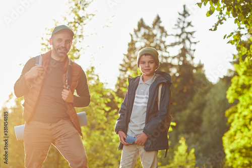 Portrait of mature father and son hiking outdoors in sunlight and looking at camera, copy space