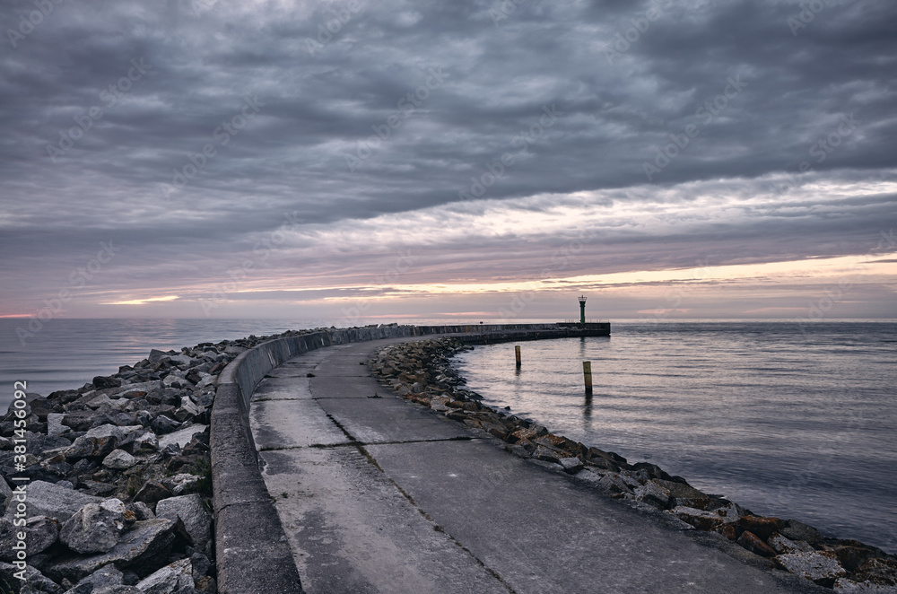 Rocky pier at sunset with dark sky, color toning applied.