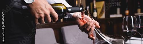 Panoramic shot of sommelier pouring wine in decanter near glasses in restaurant photo