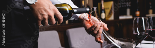 Tableau sur toile Panoramic shot of sommelier pouring wine in decanter near glasses in restaurant