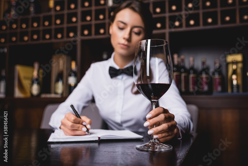 Selective focus of sommelier holding glass of wine while writing on notebook at table
