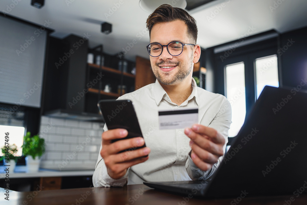 Young man holding credit card sitting in front of laptop computer at home, paying for online order. People, lifestyle, modern technologies and e-commerce concept. Online banking and shopping using mod