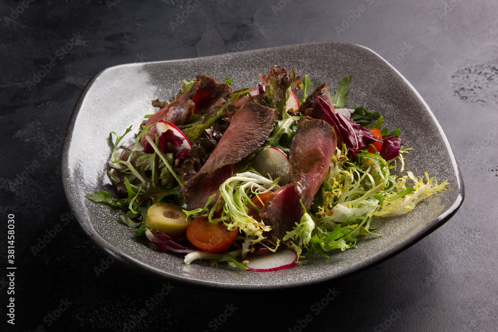 Fresh salad with frieze, tomatoes, olives, arugula, radishes and meat in a gray plate on a black background. Menu, restaurant Fresh salad with frieze, tomatoes, olives, arugula, radishes and meat in a gray plate on a black background. Menu, restaurant