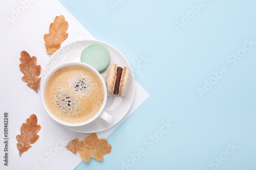 Creative autumn flat lay. Cup of coffee, macarons and oak leaves on blue background