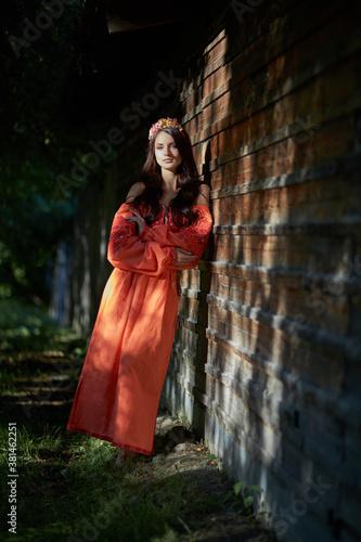 Beautiful Slavic woman in an orange ethnic dress and a wreath of flowers on her head. Beautiful natural makeup. Portrait of a Russian girl