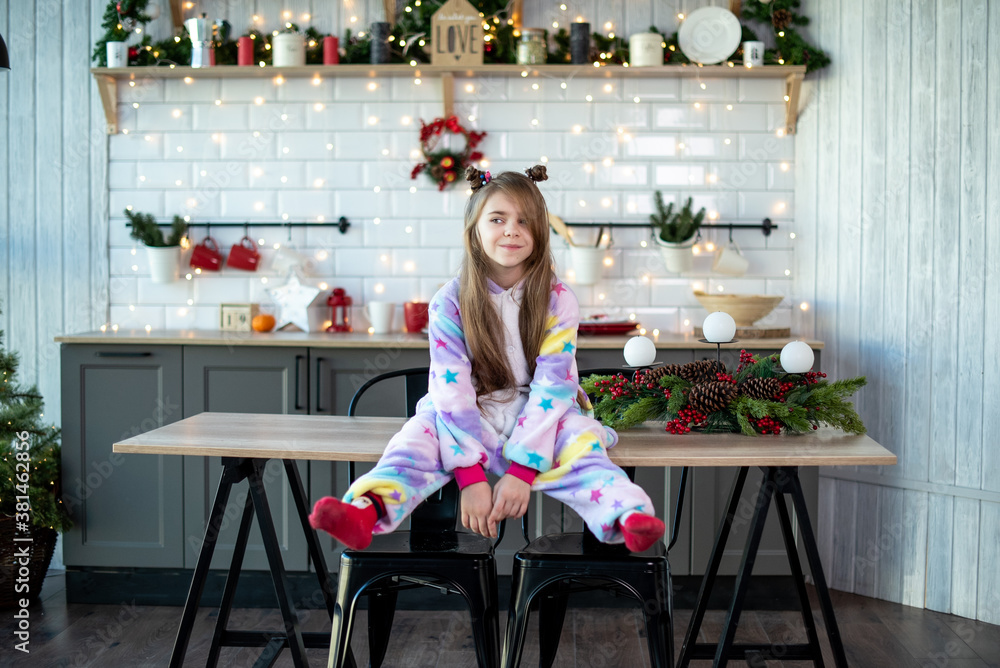 smiling toddler girl sets in the Christmas kitchen on table , Christmas decorations, lights, new year fun