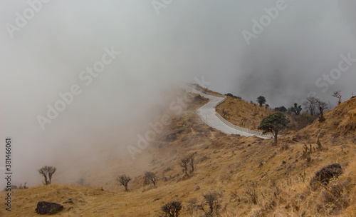 paved mountain road through valley disappearing into mist or fog.