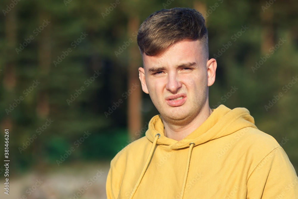 Portrait of young frustrated man with disgusted face looking at camera outdoors and wrinkle