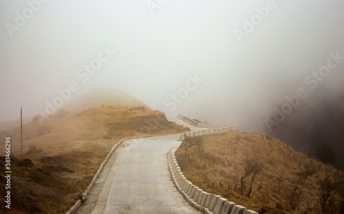 Canvas Print paved mountain road through valley disappearing into mist or fog.