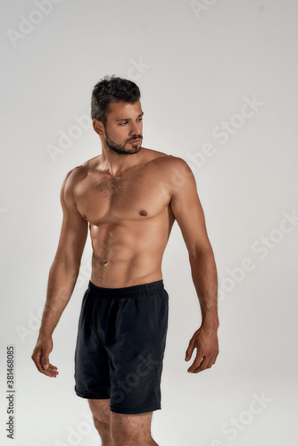 Vertical shot of a young muscular caucasian man showing his naked torso and looking away while posing shirtless isolated over grey background