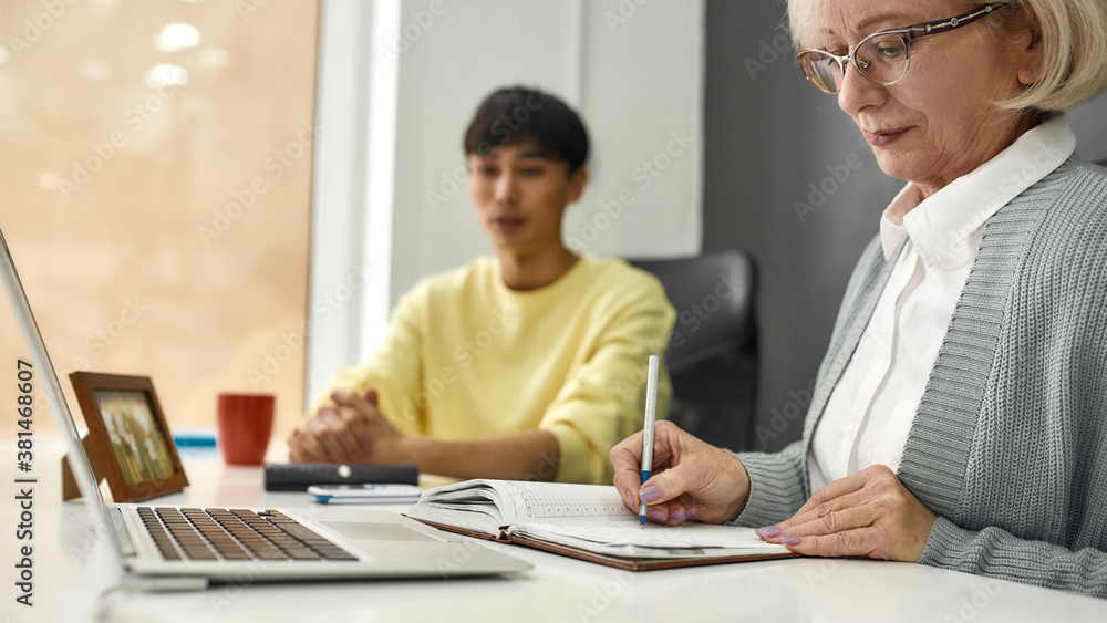Cropped shot of aged woman, senior intern making notes while listening to her young colleague, Friendly male worker training or teaching new employee