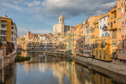 Walking Girona - Spain touristic town. Colorful yellow and orange houses and famous house Casa Maso reflected in water river Onyar, in Girona, Catalonia, Spain. © ILLYA