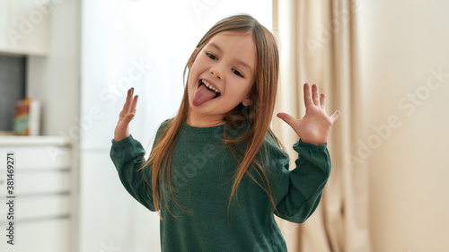 A small happy girl playing around emotionally smiling with her tongue out and her hands raised with palms open