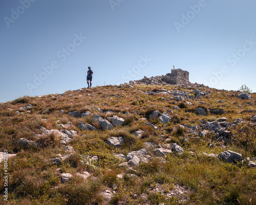 Mountain hiker walking down from Siljak summit on Rtanj mountain, old ruin at the top and autumn colored, orange grass