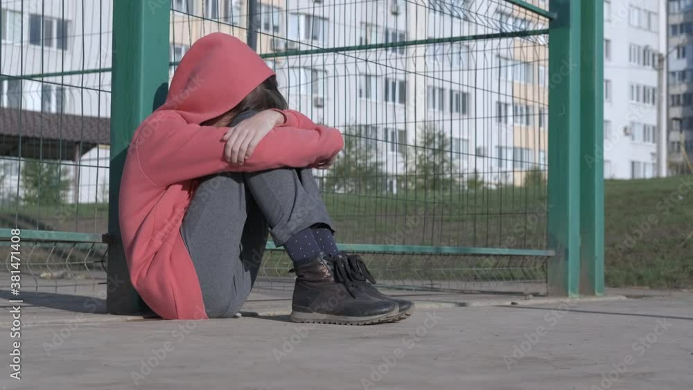 The child is depressed. Childhood loneliness. A depressed girl sits on the floor in the street. The child is depressed. Childhood loneliness. A depressed girl sits on the floor in the street.