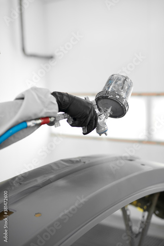young confident caucasian auto mechanic man spraying varnish at car, in protective mask and eyewear at work. automobile, car industry. wash and coating business with ceramic coating polishing