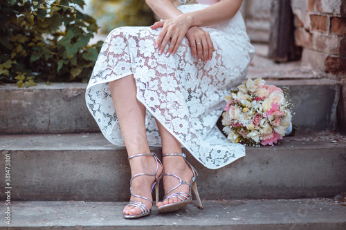 Bride sits on the stairs with wedding bouquet by her side, wearing silver sandals