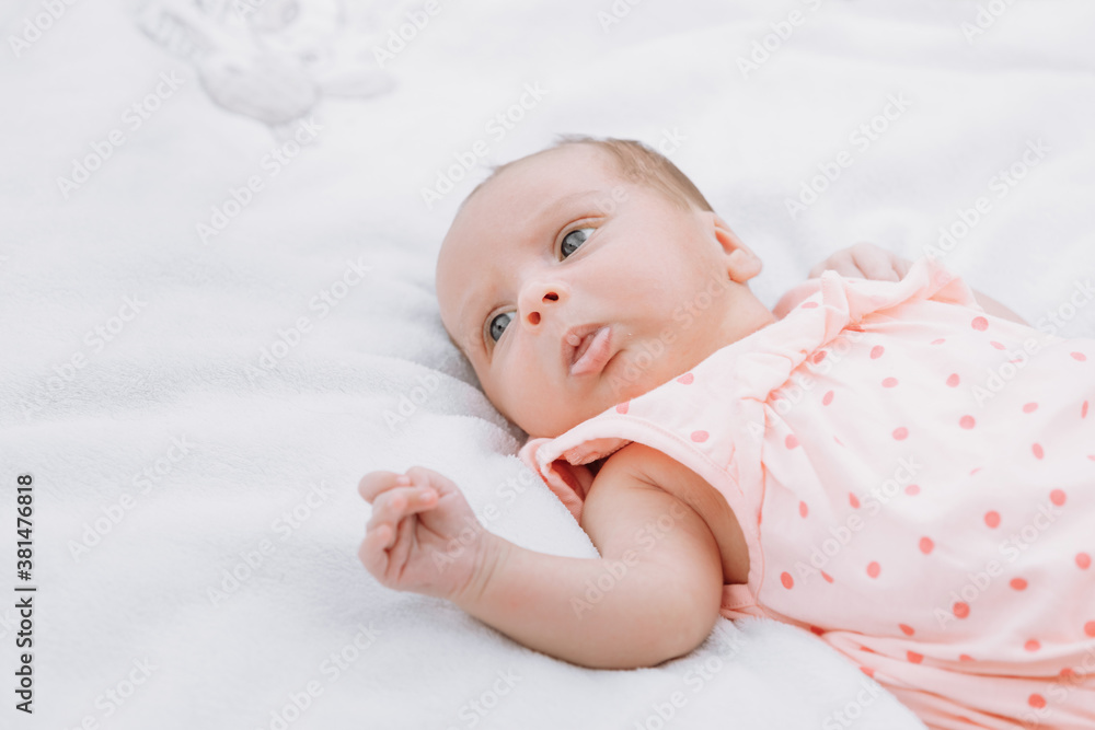 Newborn baby girl on grass in the park outdoors, lies on a white blanket looking around. selective focus.