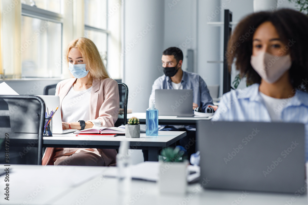 Modern coworking office with multiracial workers after quarantine. Focus on bottle with blue antiseptic on managers desk Modern coworking office with multiracial workers after quarantine. Focus on bottle with blue antiseptic on managers desk