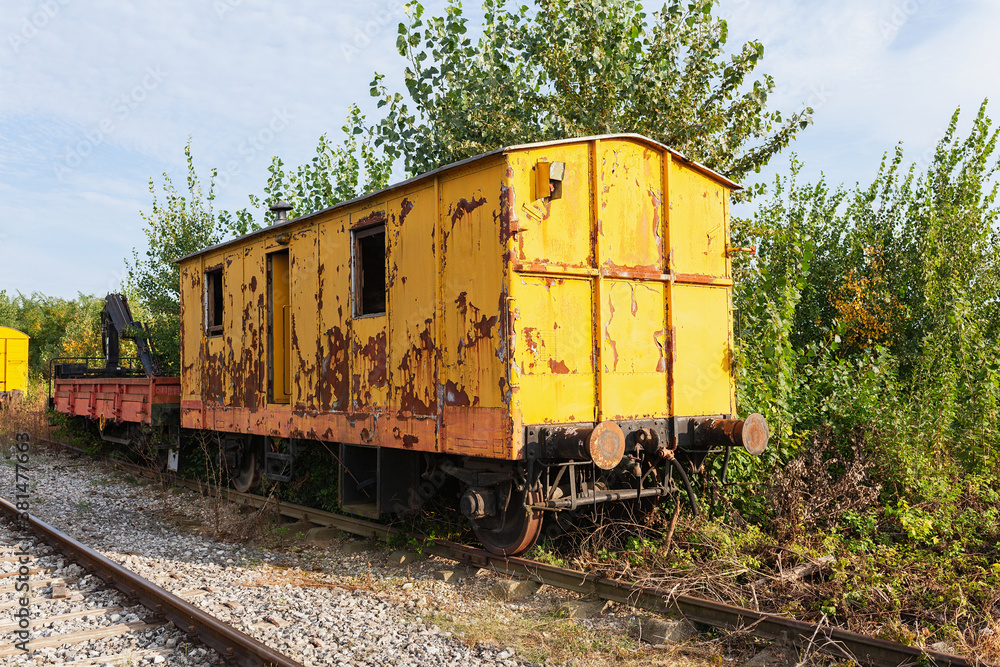 Obraz premium Old yellow train with big holes, rusty and abandoned in the field on the old tracks