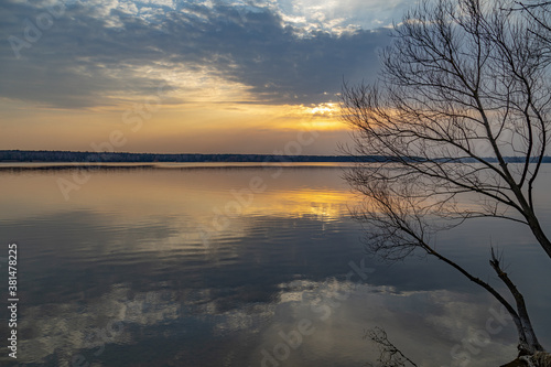 Moody evening lake landscape with sunset over water edge and sky reflecting in the water. © Garmon