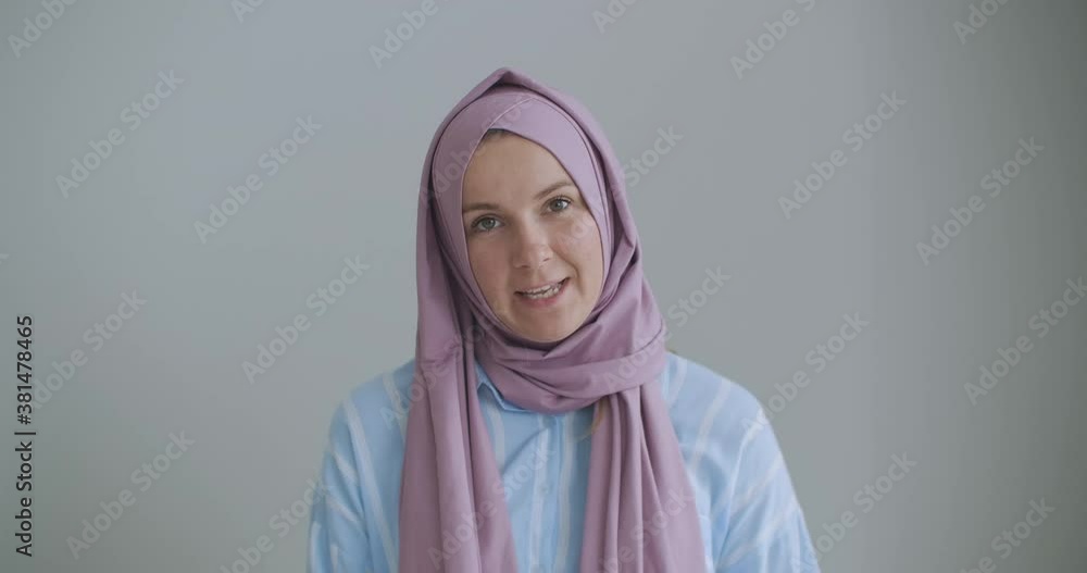 Looking at the camera muslim girl calling friends from apartments using a video link, waving with hand, sitting on a sofa in a stylish room in front of computer screen having video conversation Looking at the camera muslim girl calling friends from apartments using a video link, waving with hand, sitting on a sofa in a stylish room in front of computer screen having video conversation