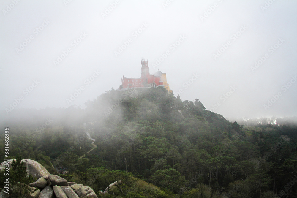 Castle standing on top of a mountain over a foggy 
 green landscape. 