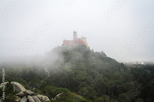Castle standing on top of a mountain over a foggy   green landscape. 