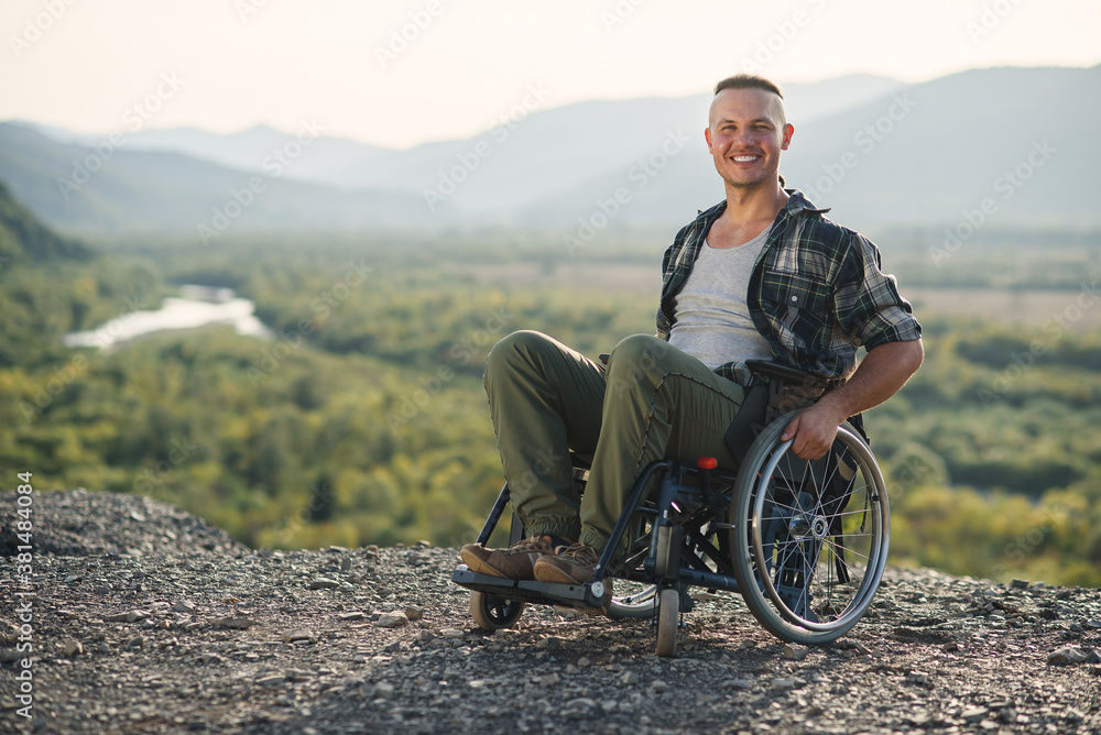 Young smiling man in wheelchair enjoying nature beauty on the mountains. People with disabilities travelling.
