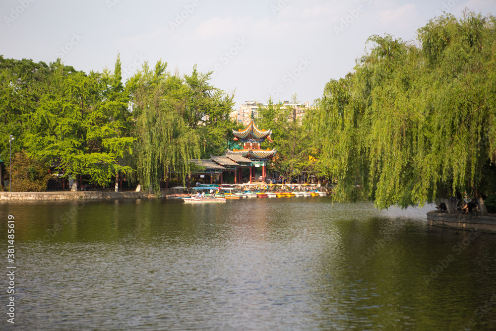 Trees and a traditional building next to a pond in a park in Kunming, China