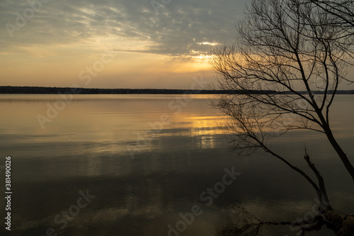 Moody evening lake landscape with sunset over water edge and sky reflecting in the water.