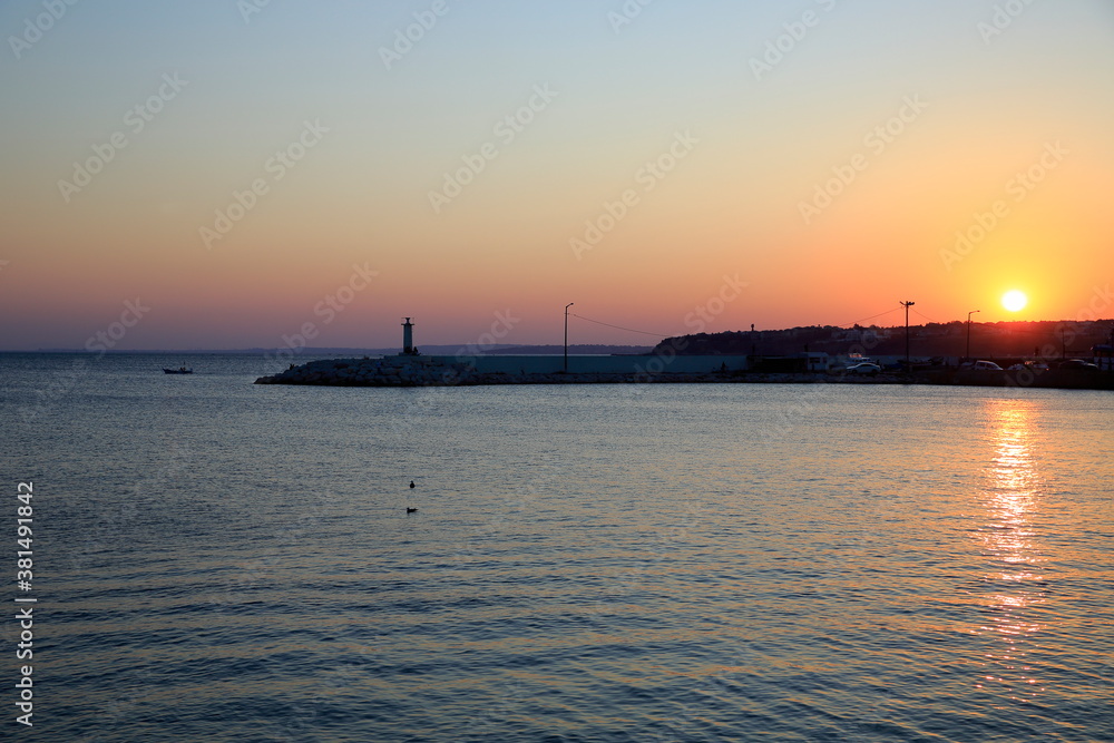 A sunset on the beach. Silivri, Turkey. City view towards the harbor and the lighthouse at a calm sunset.