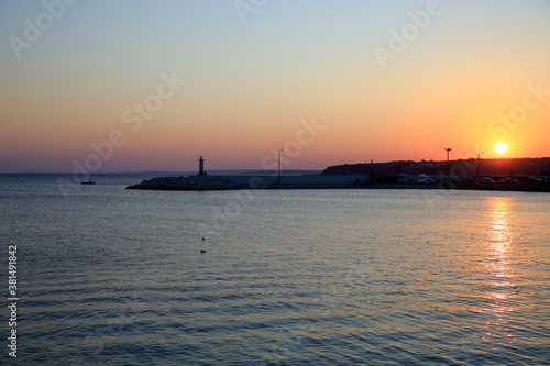 A sunset on the beach. Silivri, Turkey. City view towards the harbor and the lighthouse at a calm sunset. © Suat