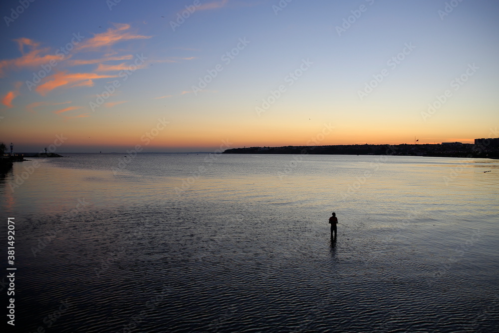 Fisherman at sunset. Man fishing in shallow water near the shore in a calm evening. Silivri, Turkey