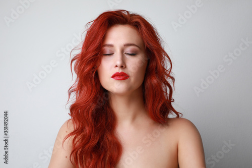 Headshot of sensual woman with closed eyes and beautiful long red hair posing over white background. Space for text.