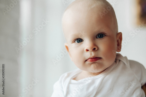 Portrait of beautiful little baby wearing in white bodysuit while looking at camera with interest. Childhood concept. Copy space © Вячеслав Косько