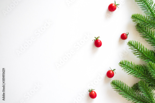 Christmas white background with fir branches and small red cherry tomatoes. Xmas, New Year's wallpaper. Winter holiday decorations isolated on white background with copy space. Flat lay, top view.
